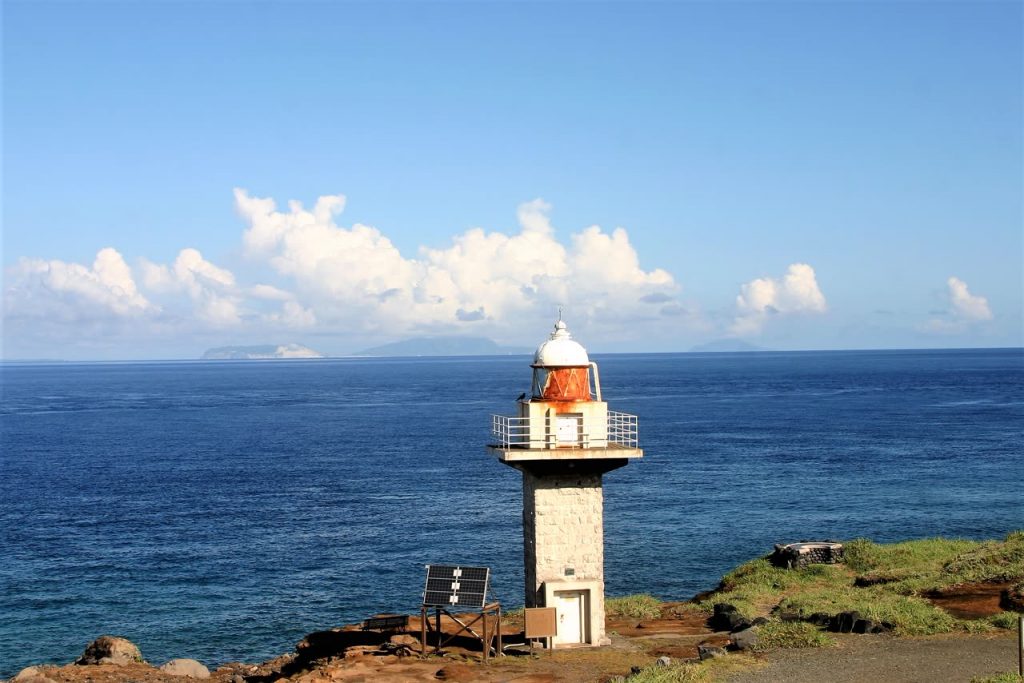 三宅島の岬に立つ灯台と、水平線に浮かぶ島影