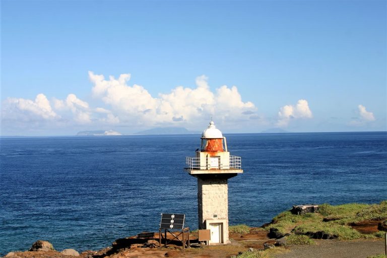 三宅島の岬に立つ灯台と、水平線に浮かぶ島影