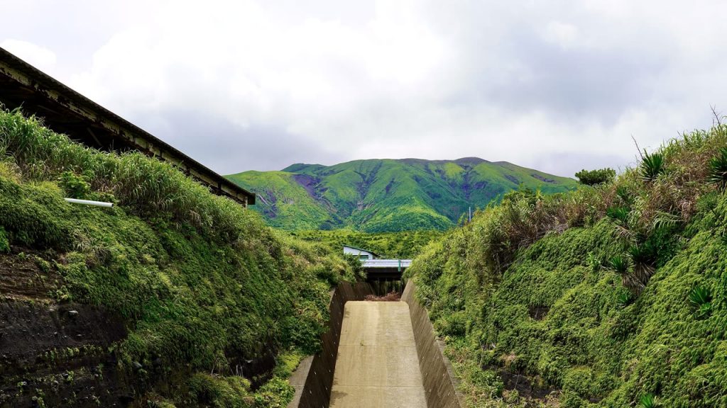 緑に覆われた山へ向かってのびるコンクリートの導流堤と、その上を渡る道路の橋