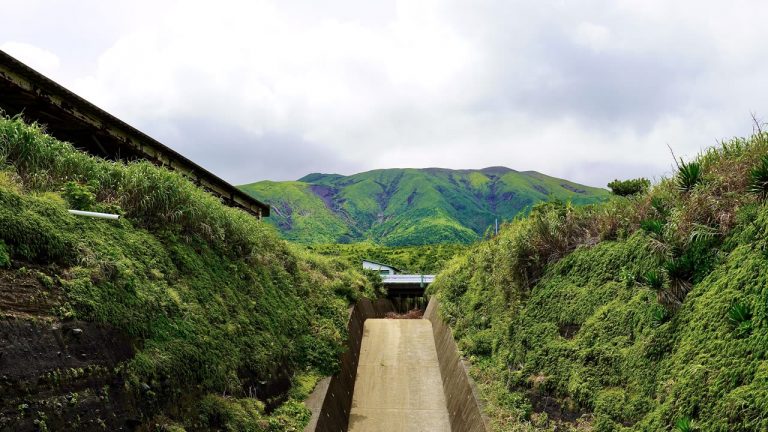 緑に覆われた山へ向かってのびるコンクリートの導流堤と、その上を渡る道路の橋