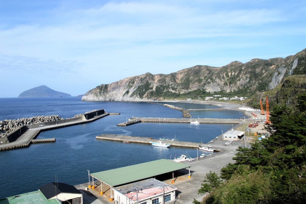 高台から見下ろす新島港の防波堤と漁船、遠くに式根島の島影