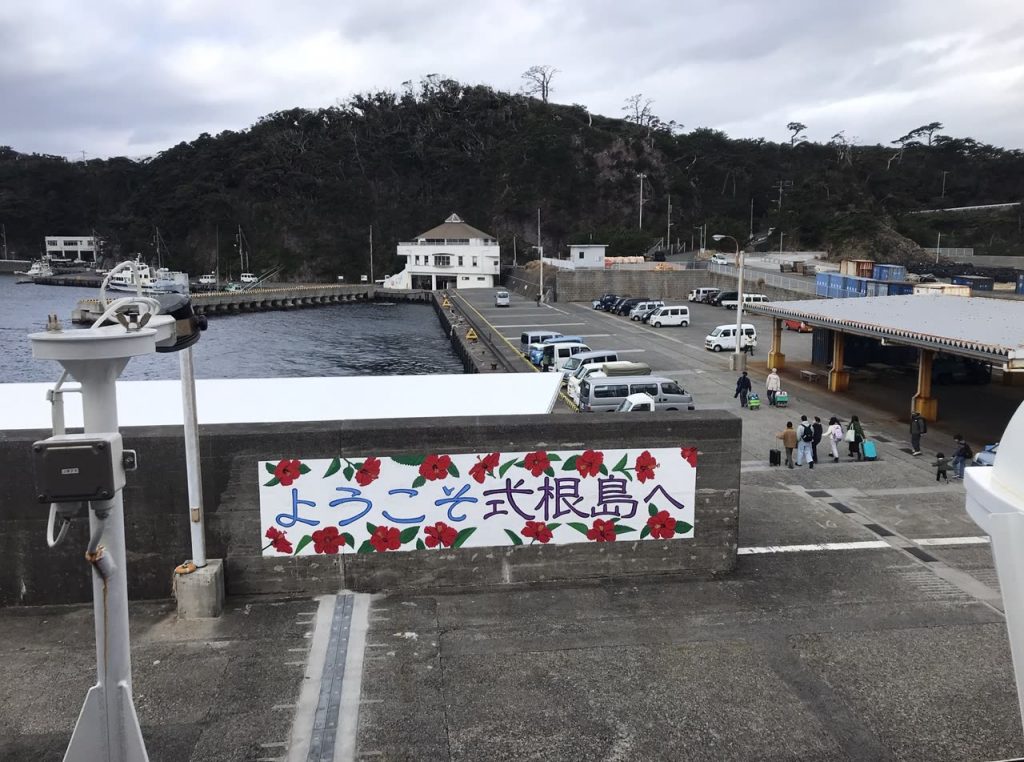 式根島の港に並ぶ送迎の車と、キャリーバッグを引いて歩く旅行者